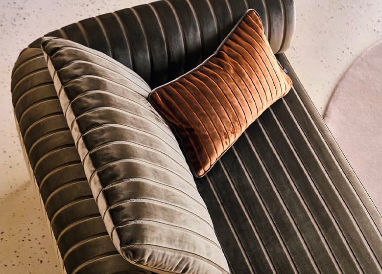 Eine Aufnahme von dem Bezug Empire Velvet auf einem Kissen und einem Sofa.