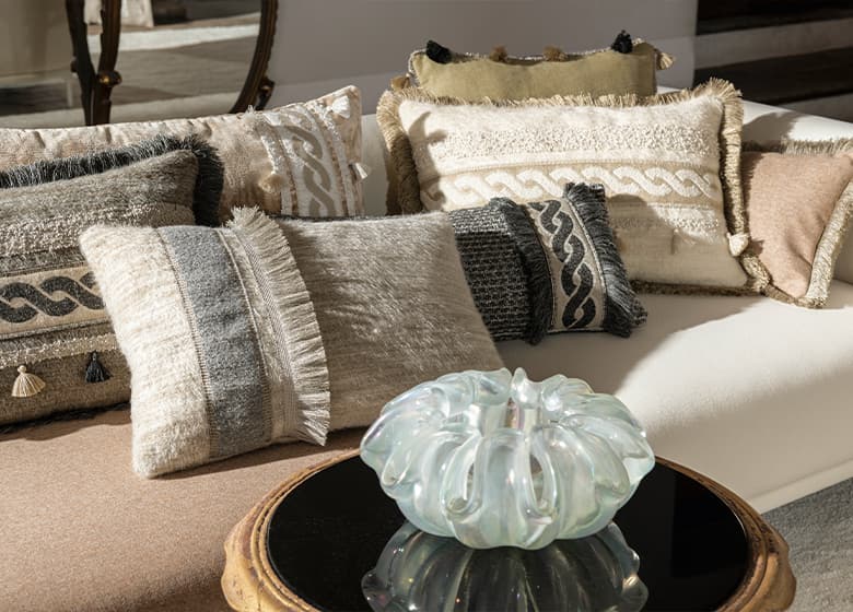 Graue und beige Kissen mit Bordüren auf einem Sofa.