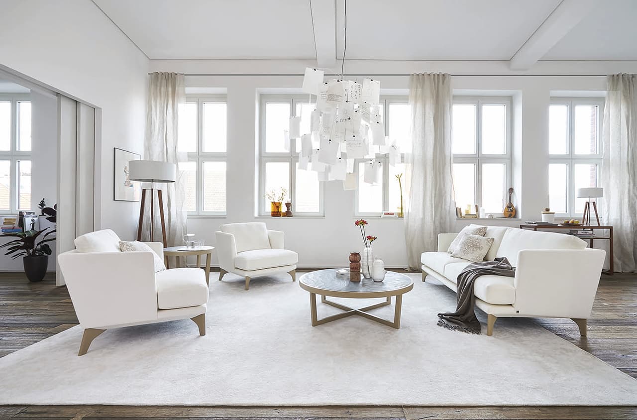 Seitenansicht eines Weißen Sofas und zweier Sessel in einem hellen weißen Raum