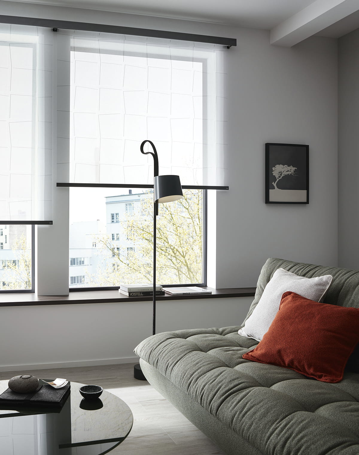 Sofa in gedecktem grün neben einer schwarzen Stehlampe und weiße Rollos mit schwarzen Schienen am Fenster