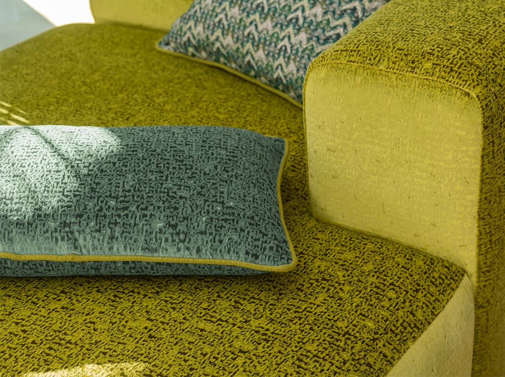 Das Bild zeigt eine Detailaufnahme von grünen Kissen auf einem gelben Sofa. Die Farben der Kissen und des Sofas werden durch schwarze Akzente unterbrochen.
