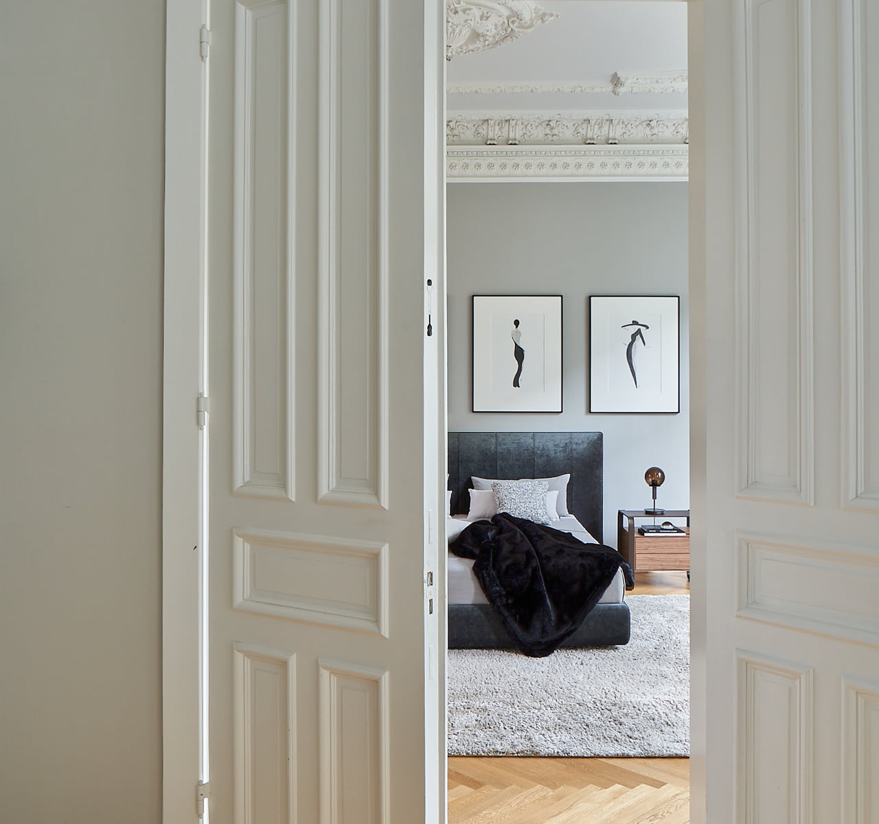 Blick durch eine geöffnete Altbau-Tür, in ein Schlafzimmer auf ein graues Polsterbett.