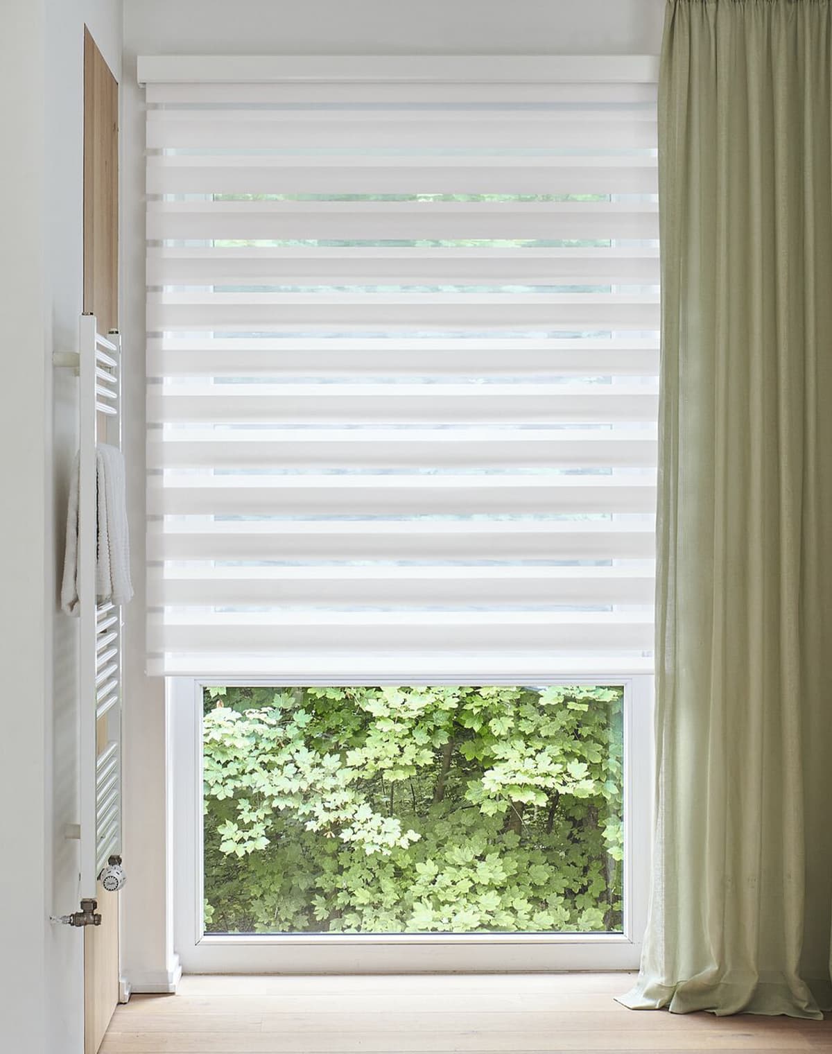 Fenster mit einem weiß gestreiftem Doppelrollo und grünem Dekoschal