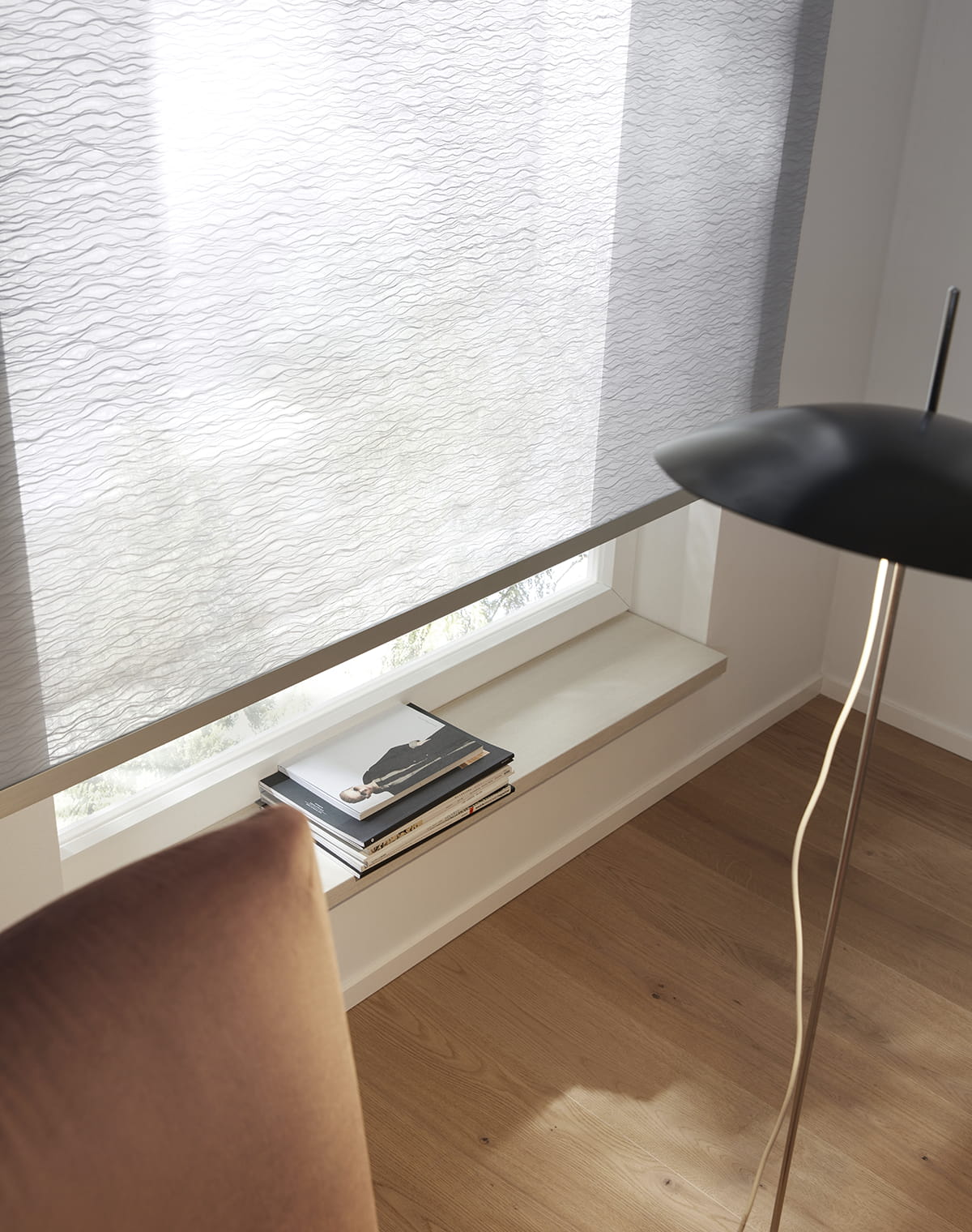 Puristische Leseecke mit braunem Sessel, schwarzer Stehlampe und einem hellgrauen Rollo mit weißem Wellenmuster am Fenster
