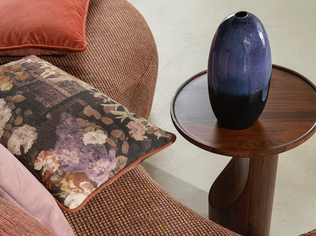 Das Bild zeigt Kissen mit floralem Print auf einer orangefarbenen Couch. Die orangen Kissen mit floralem Design schaffen eine tolle Stimmung. Ein holzfarbener Beistelltisch ergänzt die Farben der Couch harmonisch.