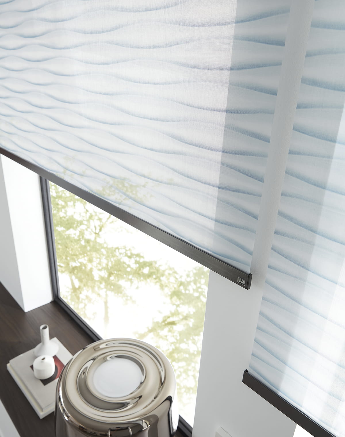 Hellblaues Rollo mit Wellenmuster auf schwarzer Schiene über einer modernen Fensterbank