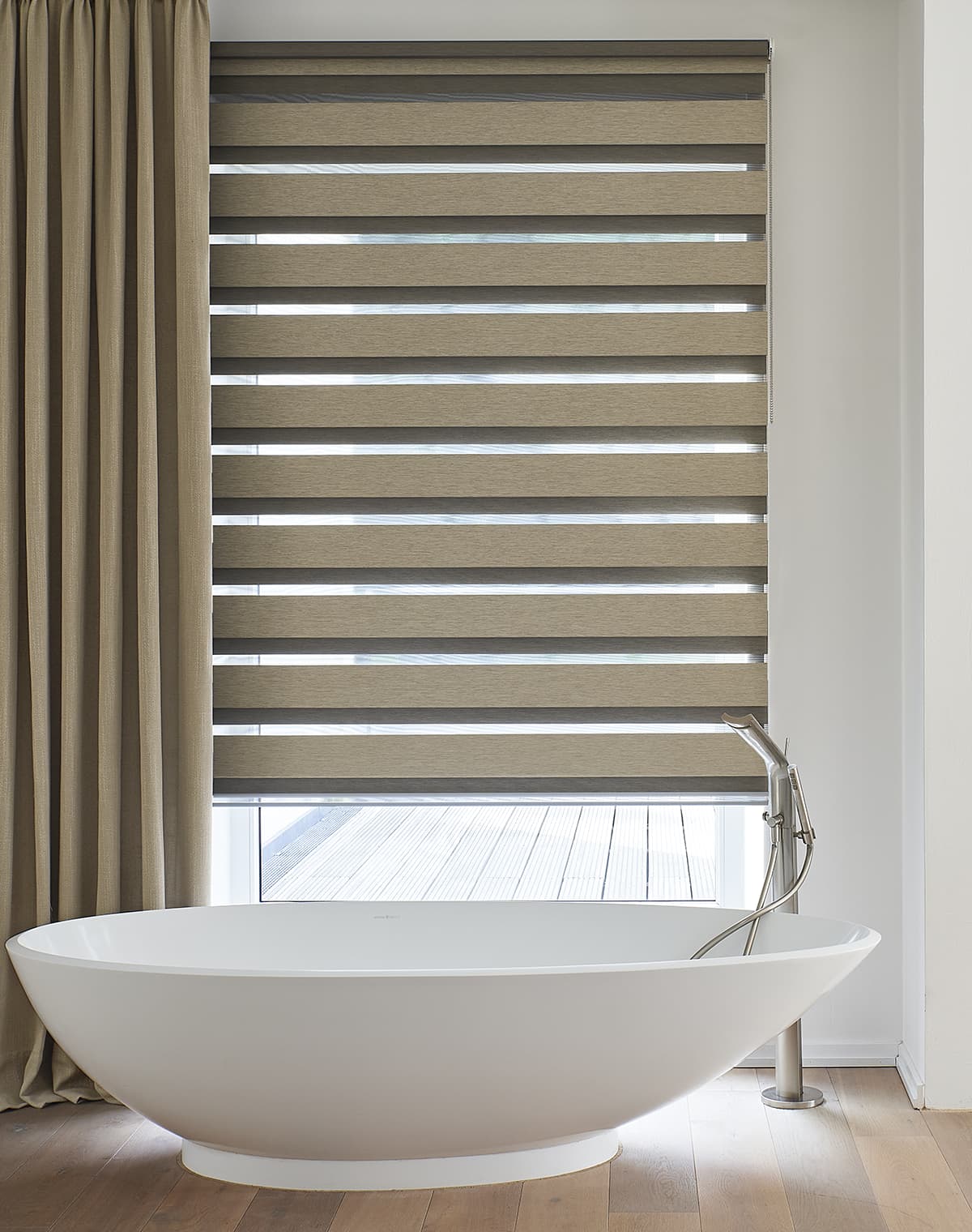 Freistehende Badewanne vor einem bodentiefen Fenster mit grau beige gestreiftem Doppelrollo und Dekoschal in beige