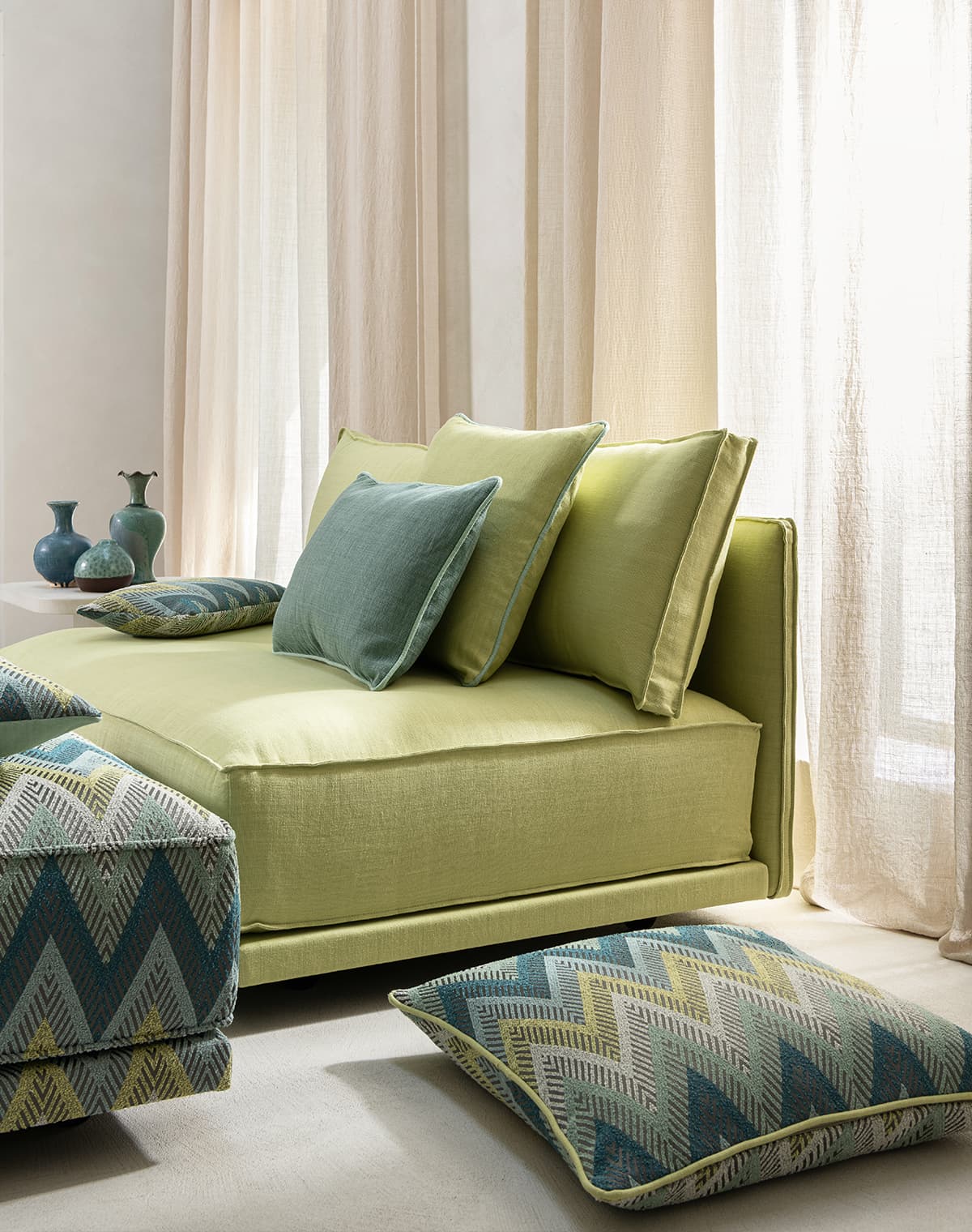 Ein grünes Sofa mit grünen Kissen vor einem beigen Vorhang.