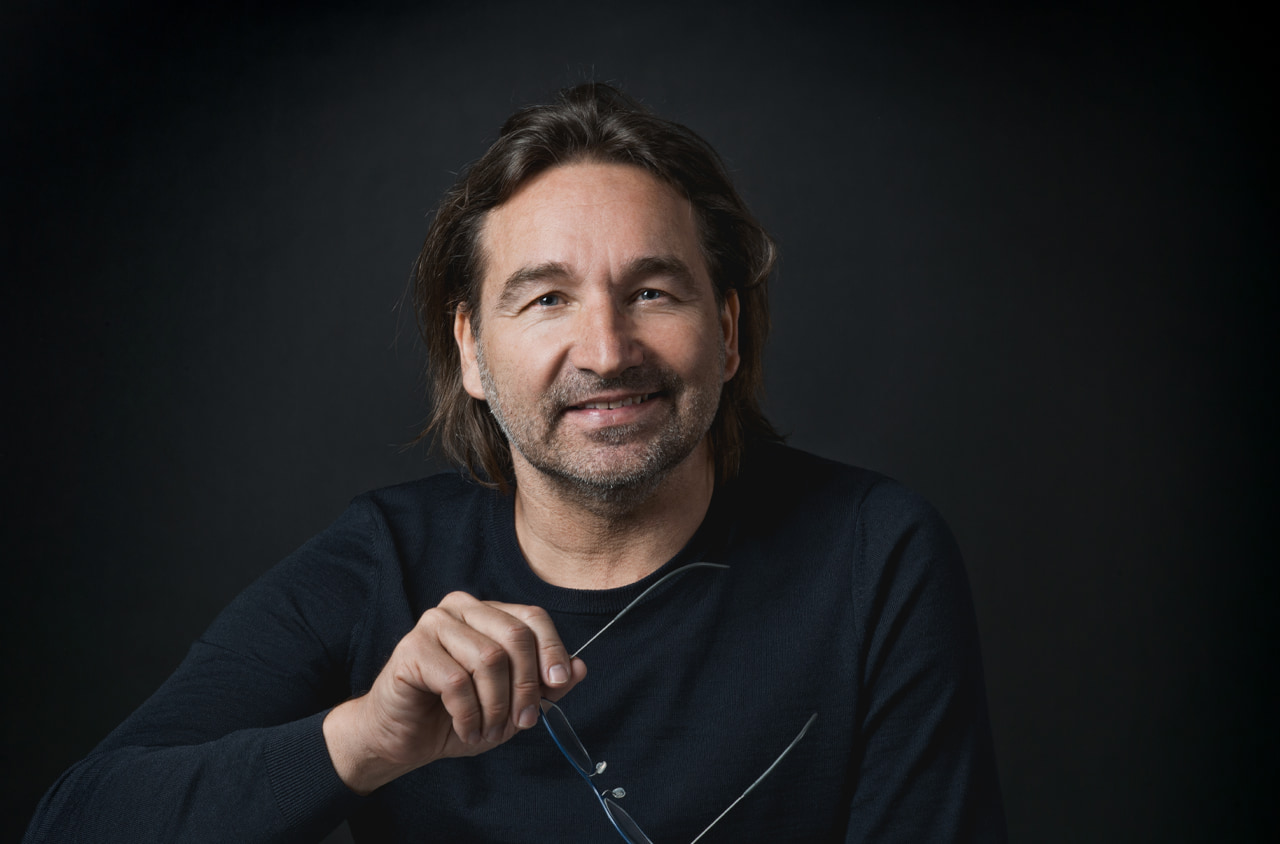 Portraitfoto von einem Mann mit braunen Haaren. Er hält eine Brille in der Hand.