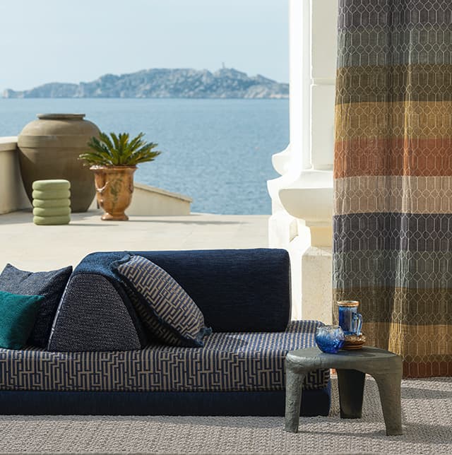 Multicolor-Vorhang und ein blaues Sofa an einer Meeresterrasse