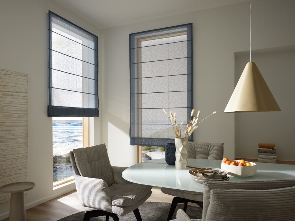 Faltrollo Light Breeze in blau in einer Raumsituation mit einem weißen Esstisch aus Glas und beige gepolsterten Stühlen und einerr beigen Lampe die über dem Tisch hängt