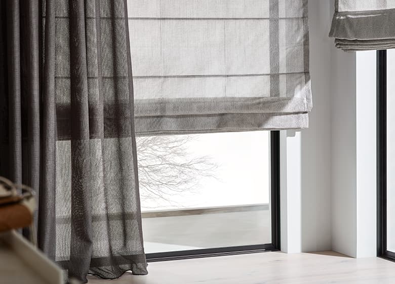 Fensterfront mit Metallrahmen und grauem Faltrollo und grauem Vorhang als Dekoration.